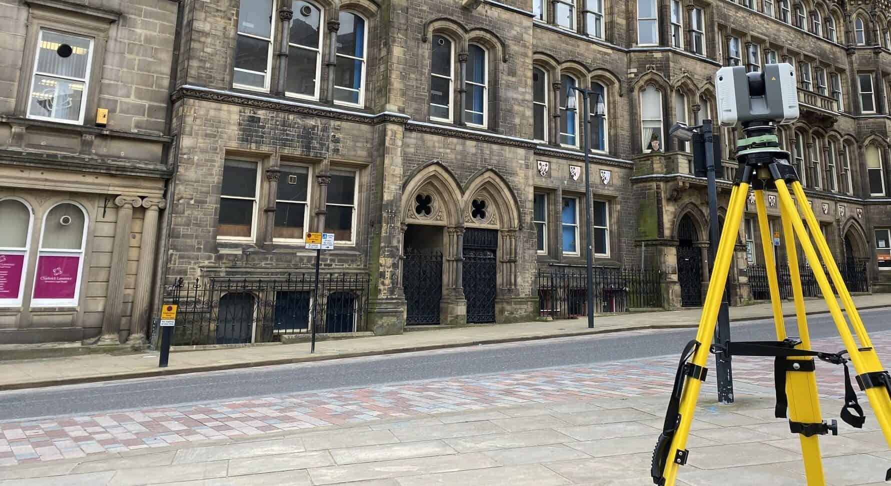 Laser scanning device set up on a city street for detailed 3D mapping and surveying, capturing precise measurements of historic building facades.